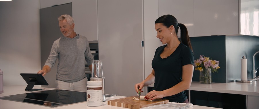 A man and woman prepare a meal in the kitchen while using a control system touchscreen.