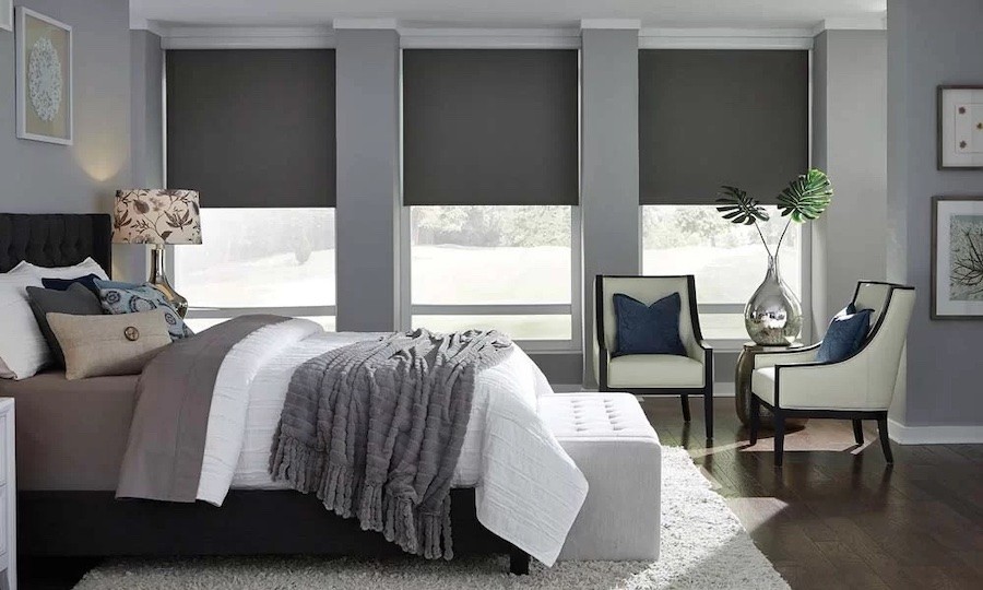 Lutron blackout shades in a bedroom with three windows and a large bed with a seating area.