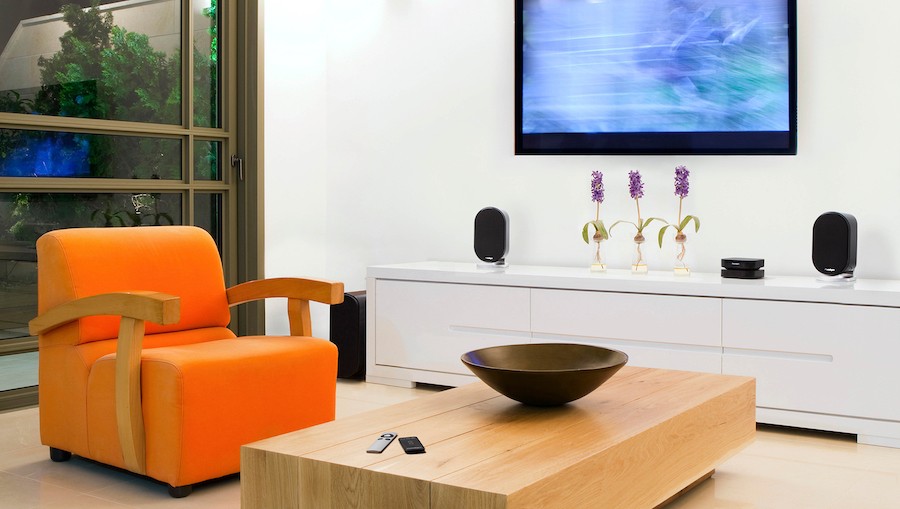 orange chair and light wood coffee table in front of a TV and TV stand with Paradigm speakers on it.