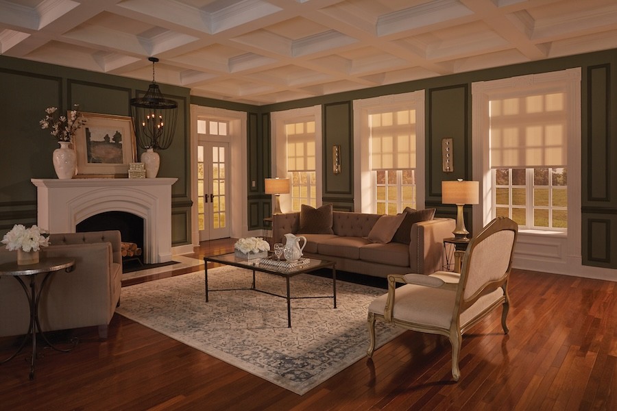 Electric shades are open half-way at dusk to allow natural light inside a cozy living room with a fireplace.