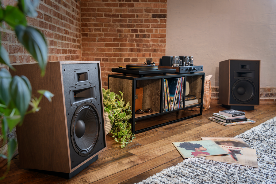 Klipsch speakers on the floor on either side of a table holding a record player with vinyls strewn across the floor.