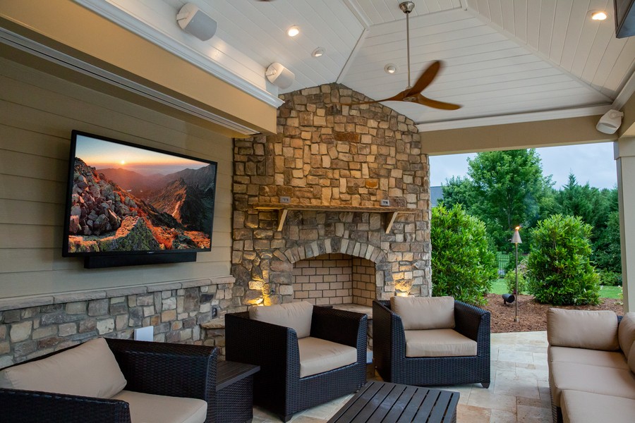 A home’s patio with an outdoor SunBrite TV, in-ceiling speakers, and fireplace.
